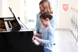 Seorang anak sedang belajar piano dengan guru privat di rumah, mencerminkan pembelajaran yang fokus dan menyenangkan